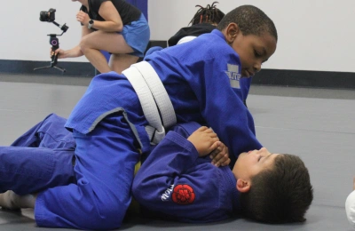 Children practicing Brazilian jiu-jitsu while an instructor provides guidance during class.