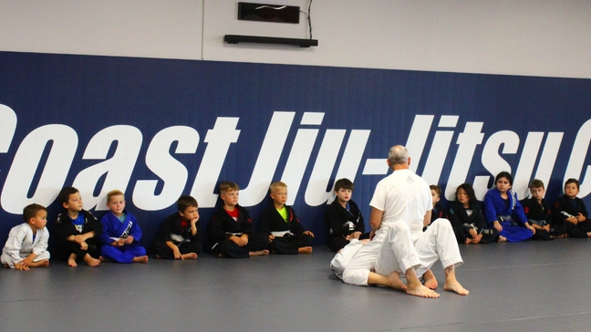 Kids Jiu-Jitsu class listening to instructor on the mats